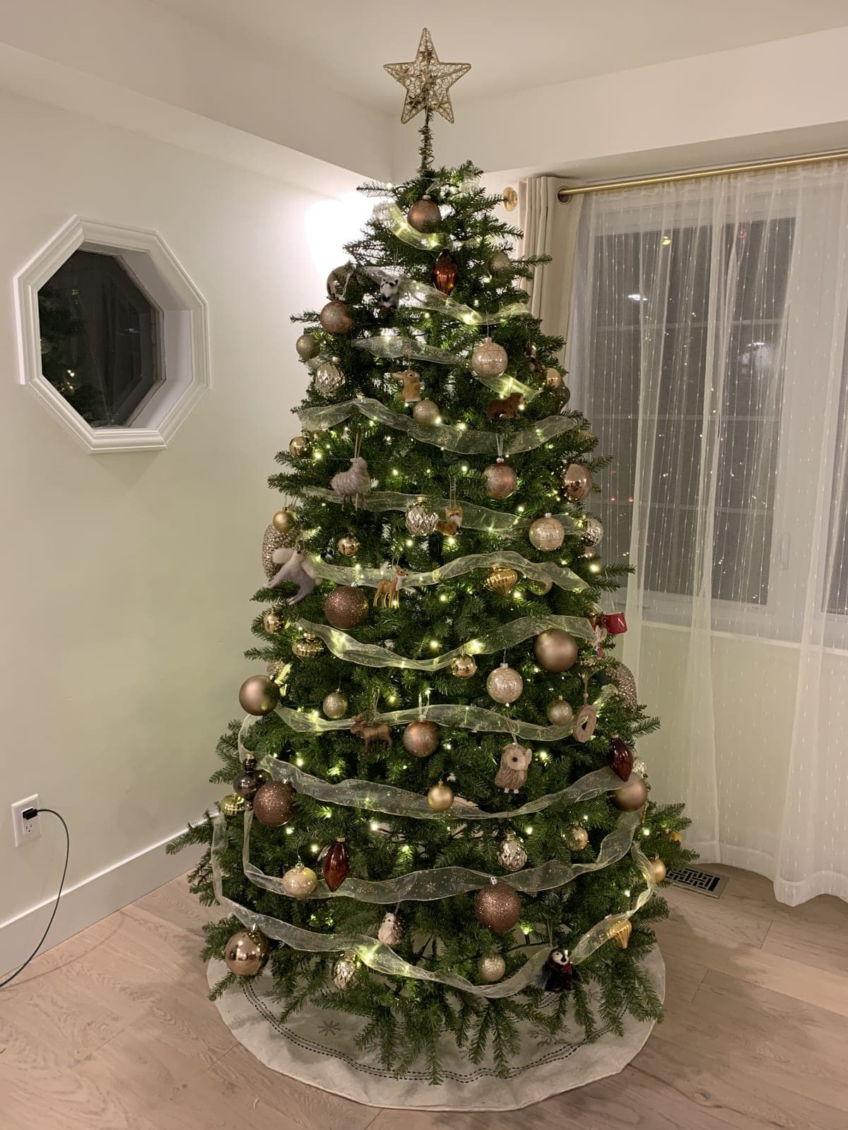 Decorated Christmas tree with warm-white lights and sheer ribbon garland in a bright corner