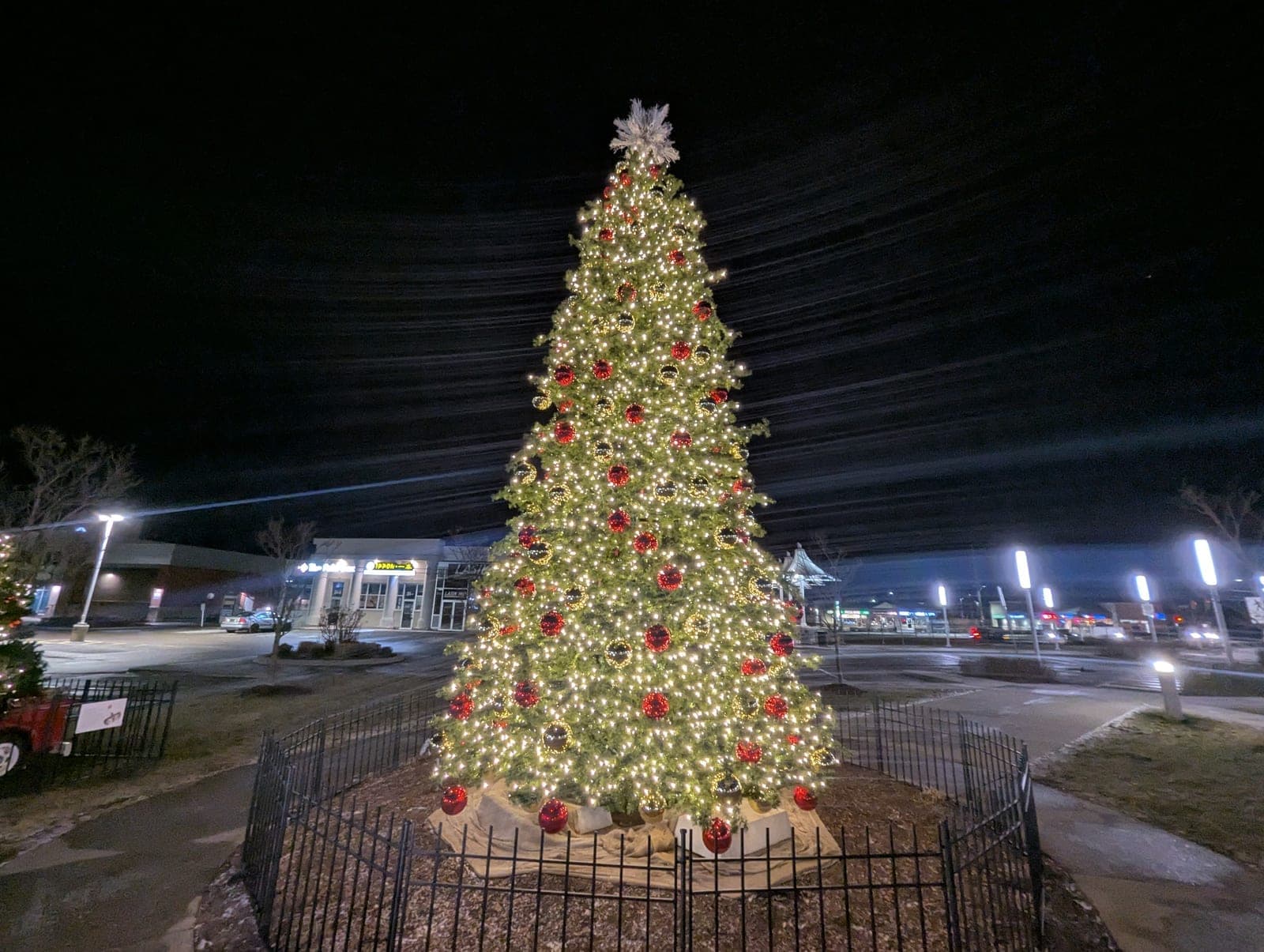 Large decorated commercial Christmas tree with warm-white lights in a shopping plaza at night
